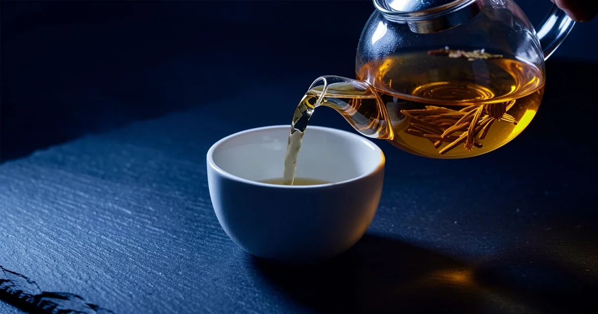 Teiera in vetro che versa tè amber in una tazza